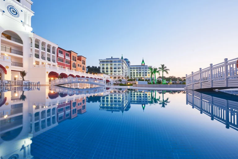 TourDent partner hotel Amara Dolce Vita luxury resort pool reflecting illuminated buildings at dusk