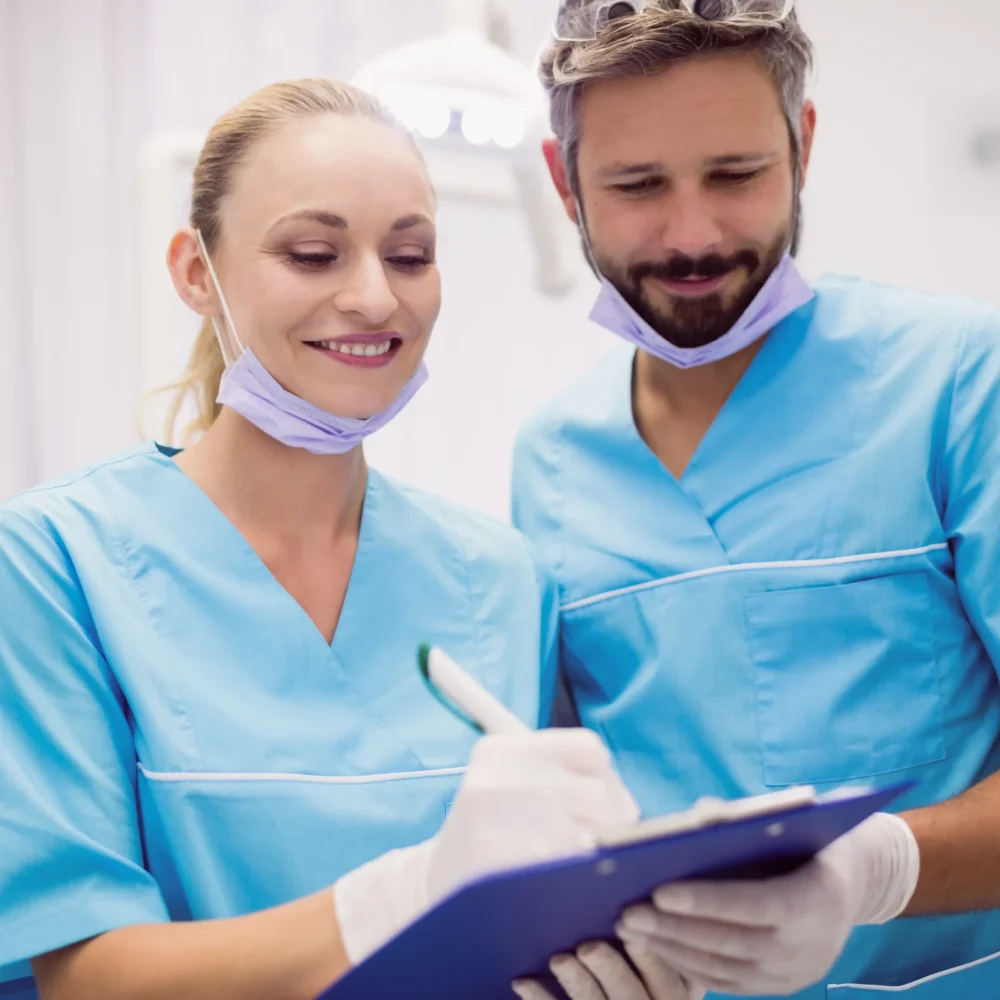 TourDent male and female dentists in scrubs reviewing patient records on clipboard in dental clinic